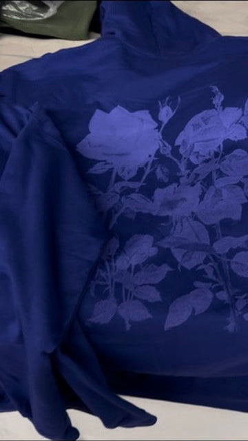 A dark blue long-sleeve top with a tonal dark blue floral rose pattern on the front, laid flat on a light surface.